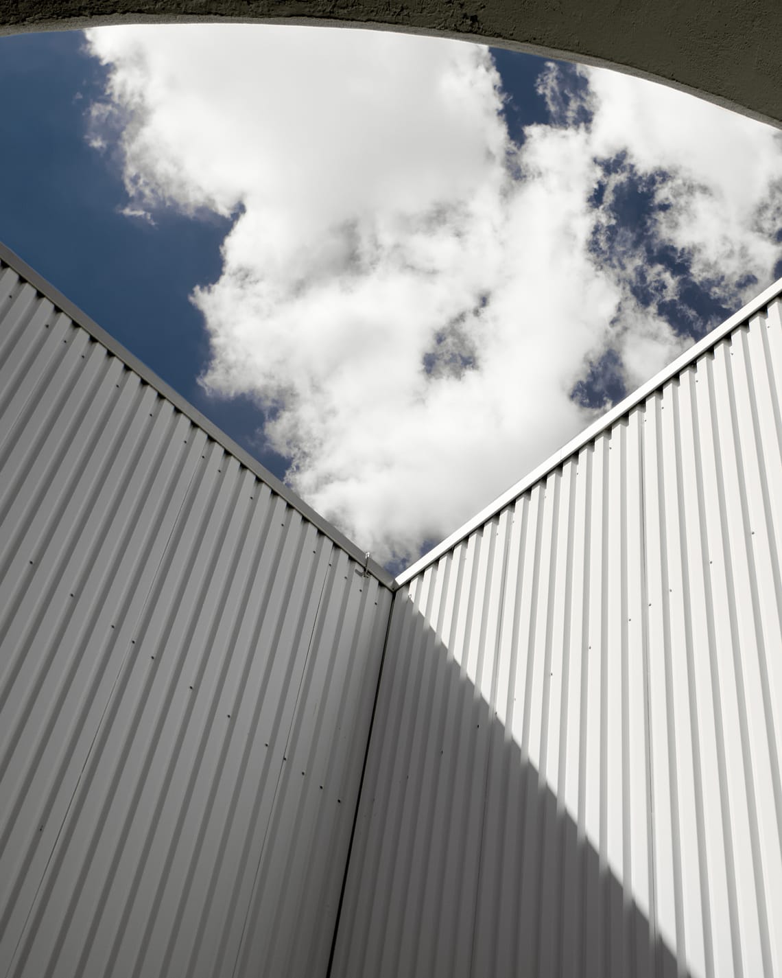 white clouds on blue sky. simple windowsless architecture is framing the image. 